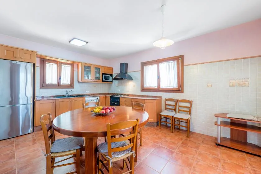 Una cocina con armarios de madera, una mesa redonda y suelo de baldosas.