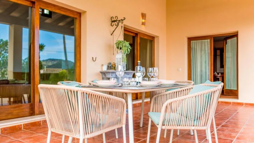 Un comedor en una terraza cubierta con la mesa puesta y asientos tejidos.