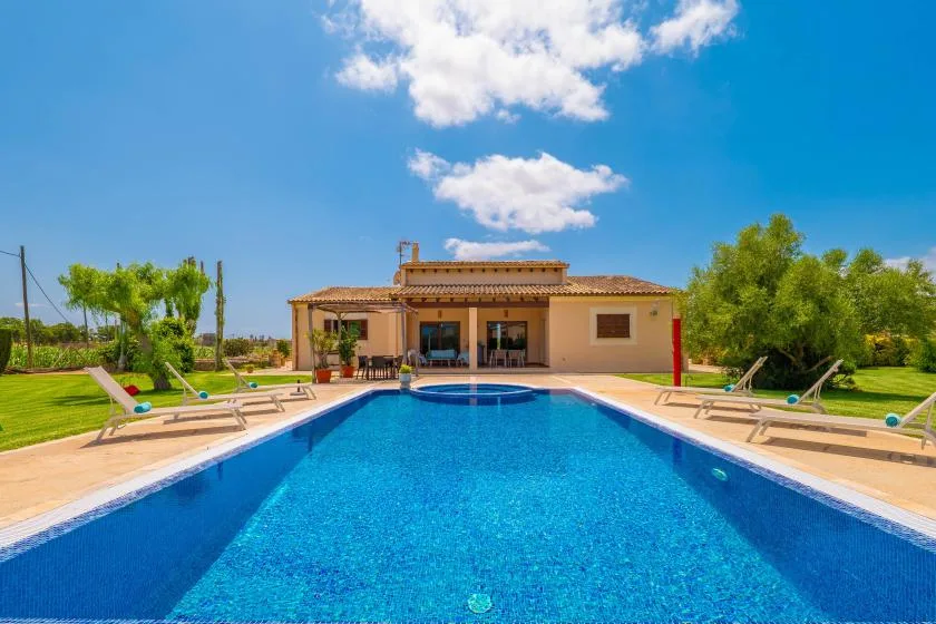 Una piscina se extiende hacia una casa baja, con tumbonas alrededor.