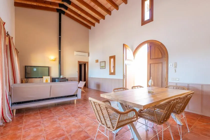 Un luminoso salón-comedor con mesa y asientos bajo vigas de madera a la vista.