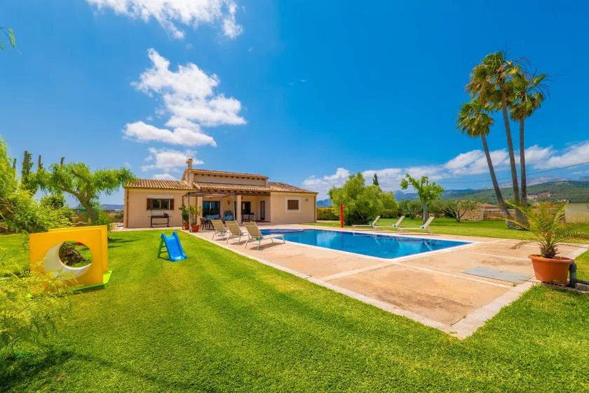 Una casa y una piscina están junto a un césped bajo un cielo azul despejado.