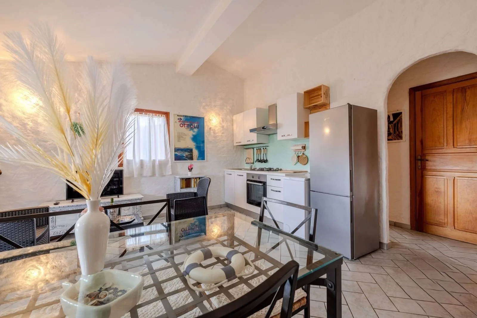 Un comedor con una mesa de vidrio está junto a una cocina compacta.
