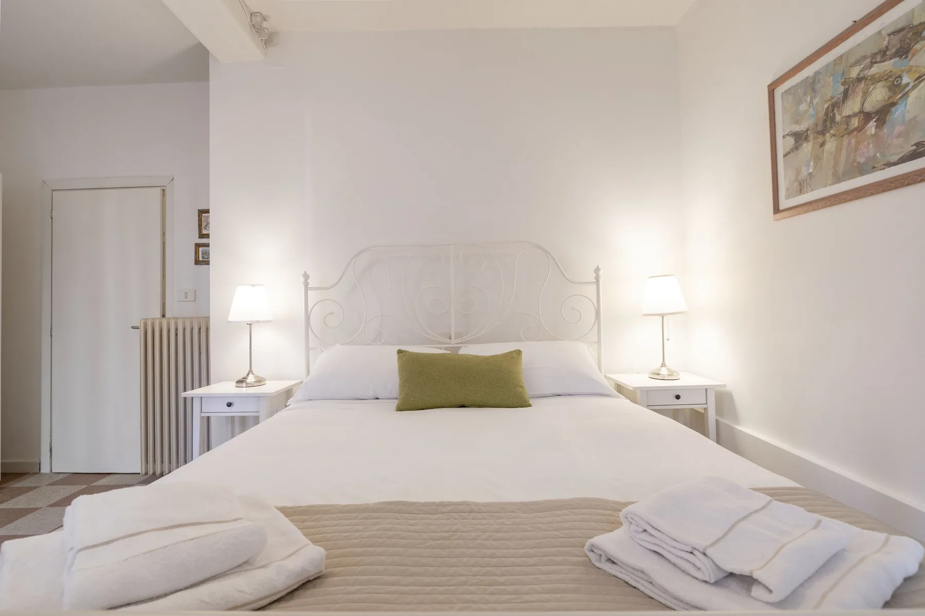 Un dormitorio con una cama bien hecha, mesitas de noche y un cuadro enmarcado.