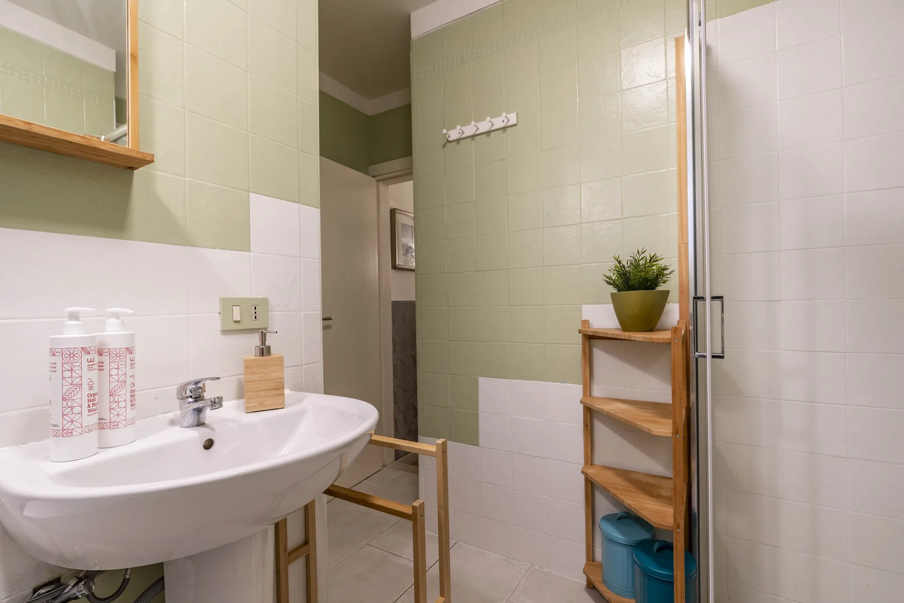 Un baño alicatado con lavabo, ducha y estantería de madera.