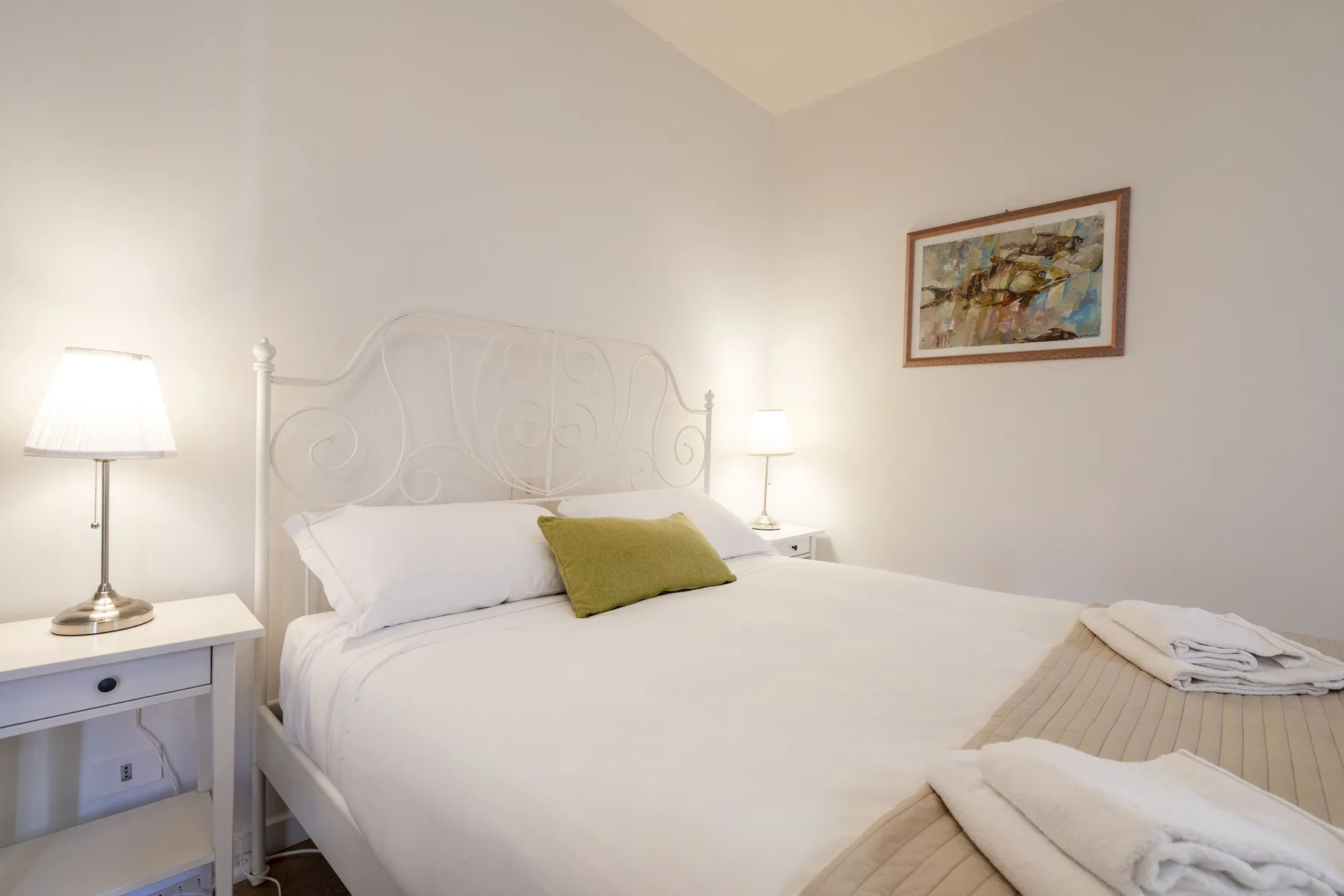 Un dormitorio luminoso con una cama bien hecha, lámparas de noche y un cuadro en la pared.