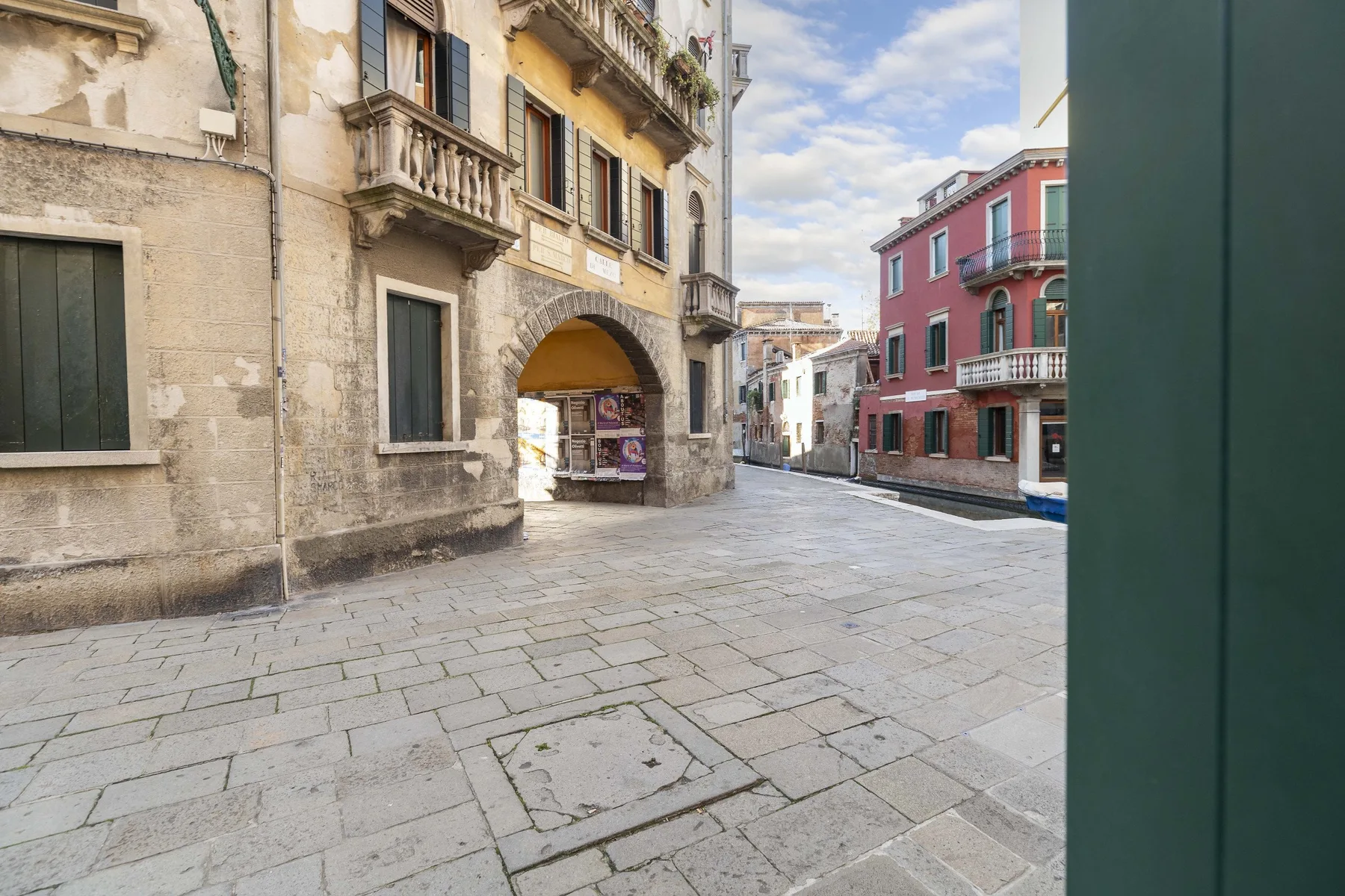 Una calle peatonal pavimentada pasa entre edificios de piedra y una fachada roja.