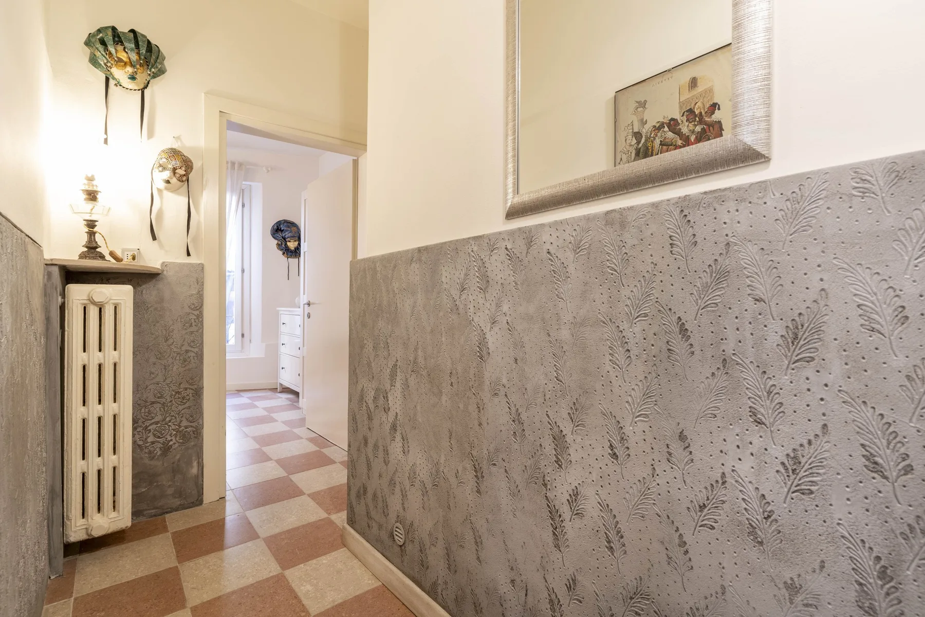 Un pasillo estampado con suelo de baldosas y un radiador bajo una lámpara de pared.
