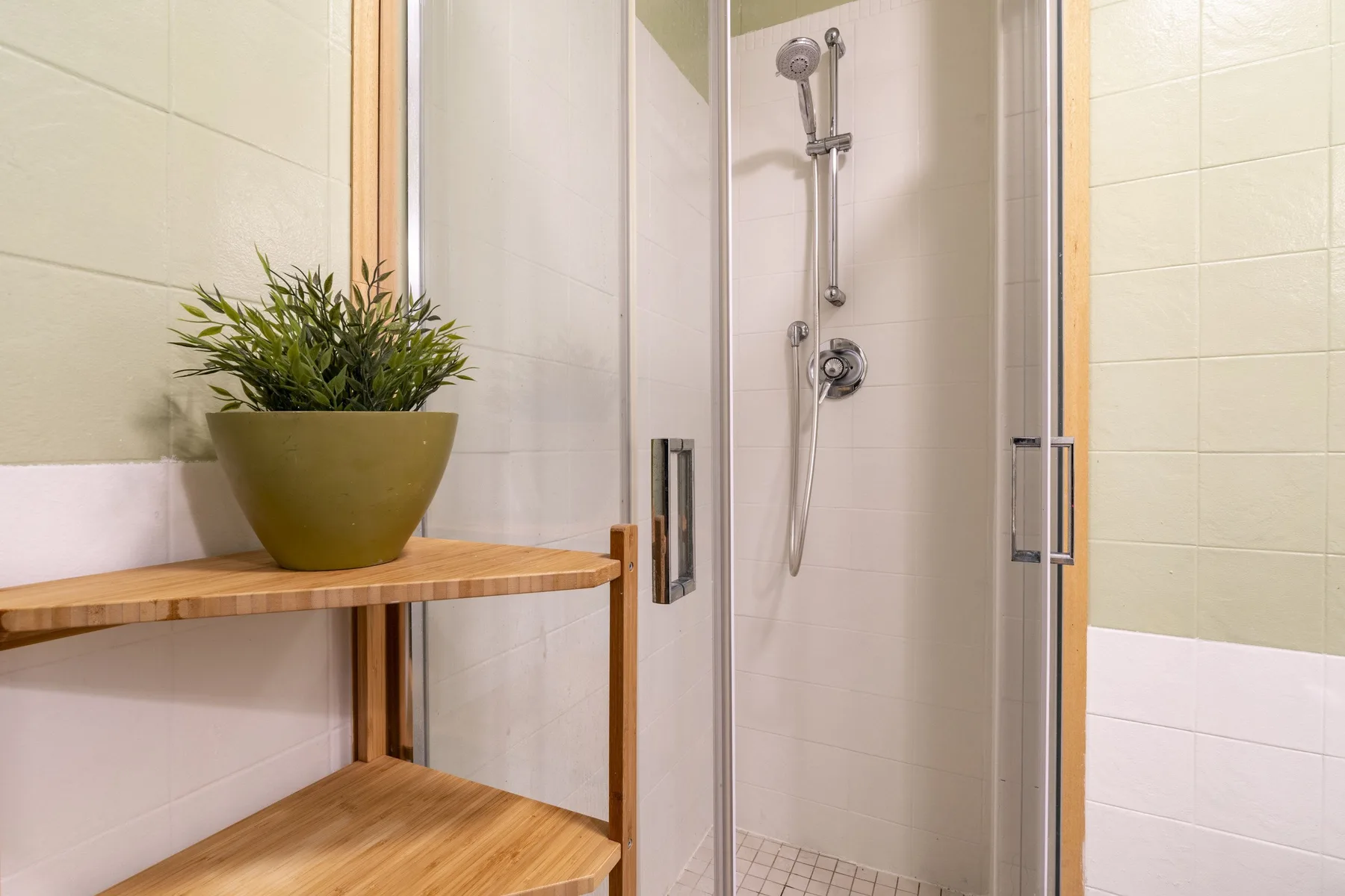 Un baño con azulejos, una ducha de vidrio y una repisa de madera con una planta.