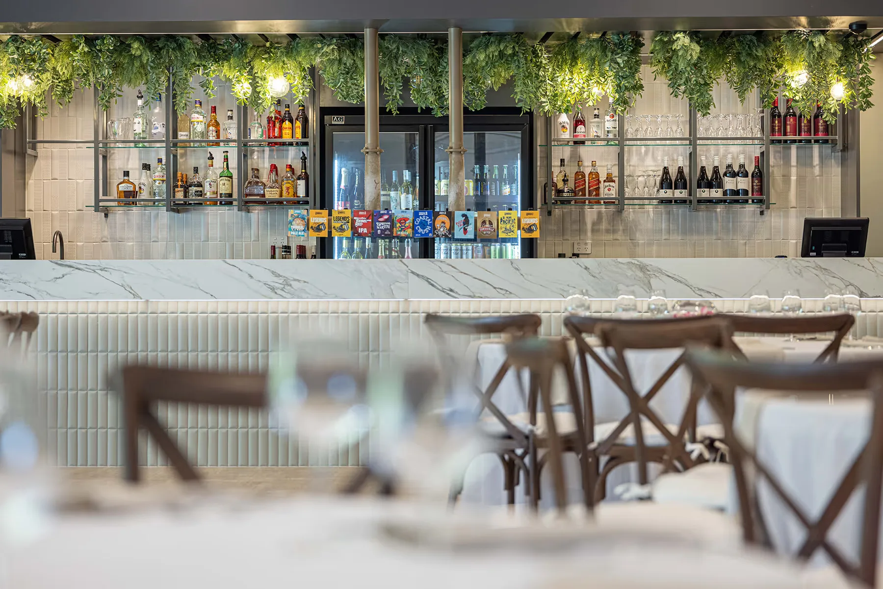 El bar del hotel, con taburetes de respaldo cruzado y vegetación colgante.
