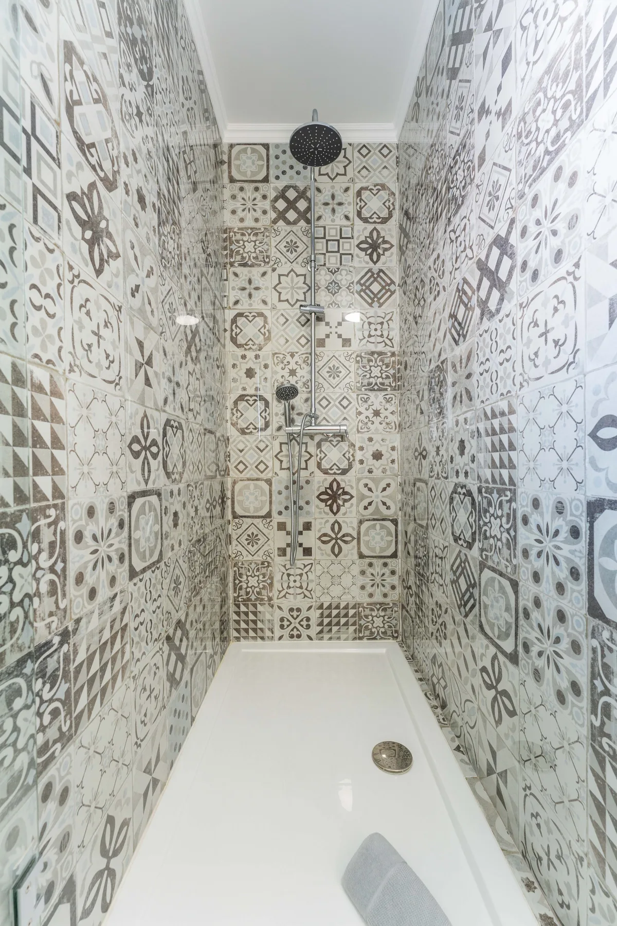Una ducha con paredes de azulejos estampados y un suelo blanco.