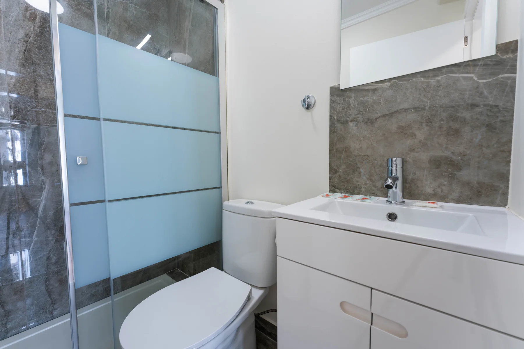Baño con ducha de vidrio, inodoro y mueble con lavabo.