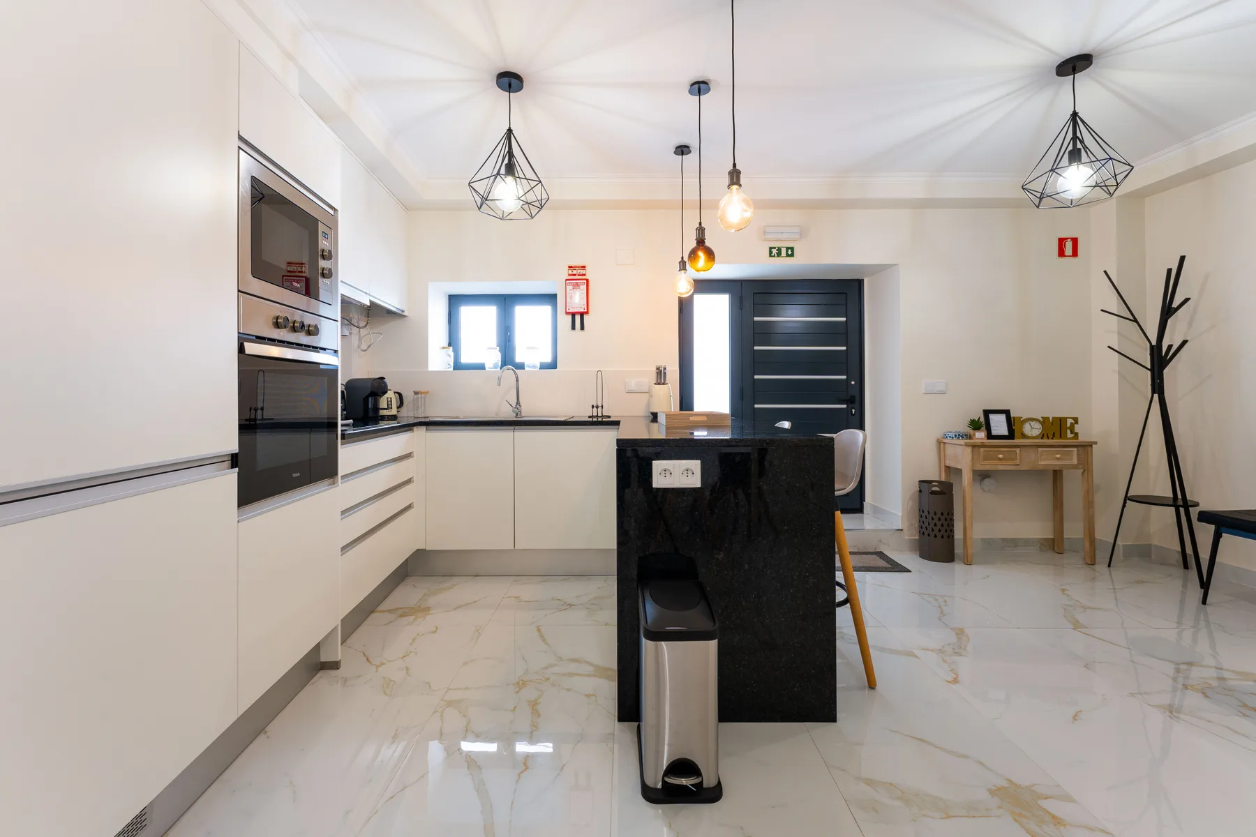 Una cocina luminosa con isla, gabinetes blancos y lámparas colgantes.