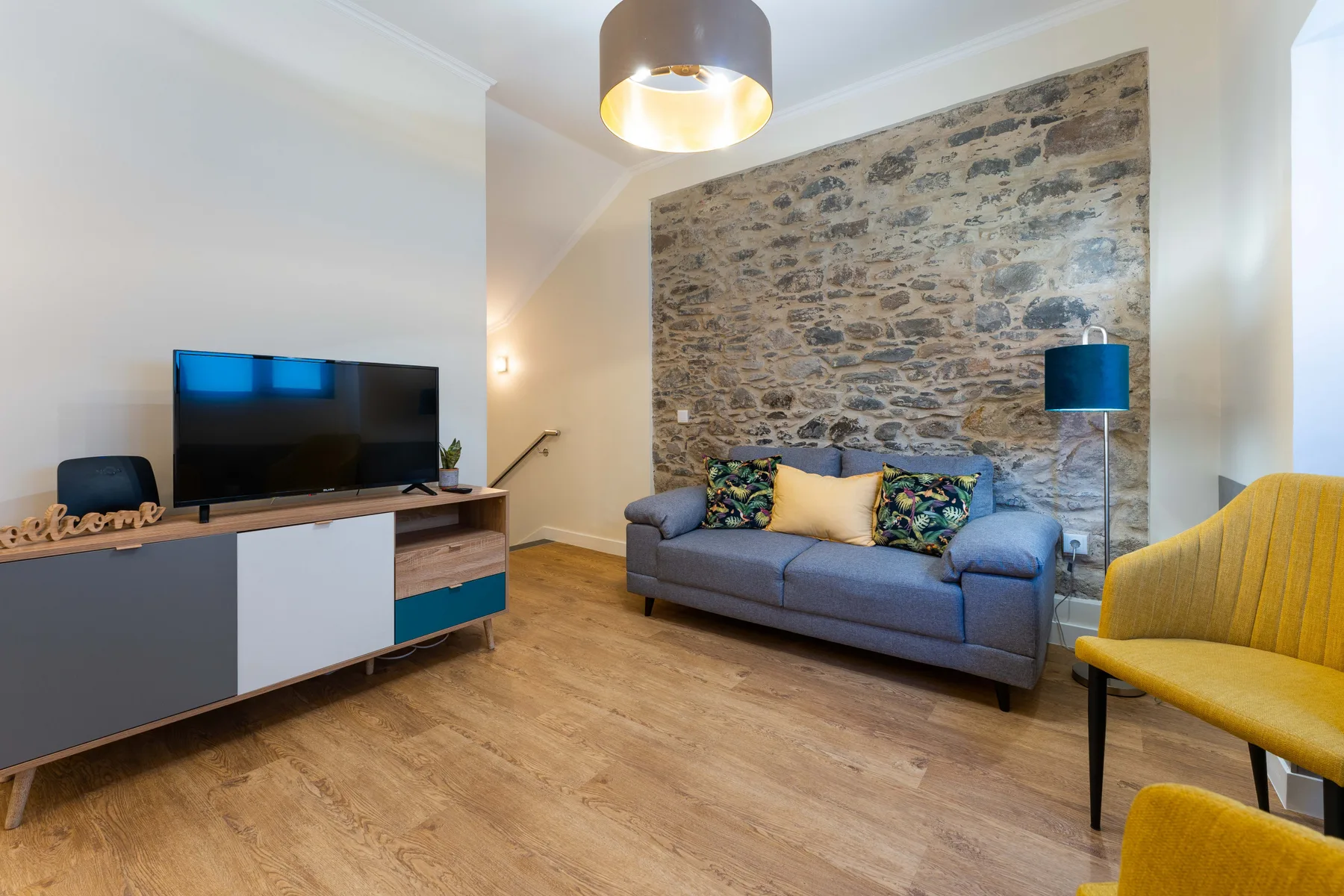 Una sala de estar con sofá, televisor y una pared decorativa de piedra.