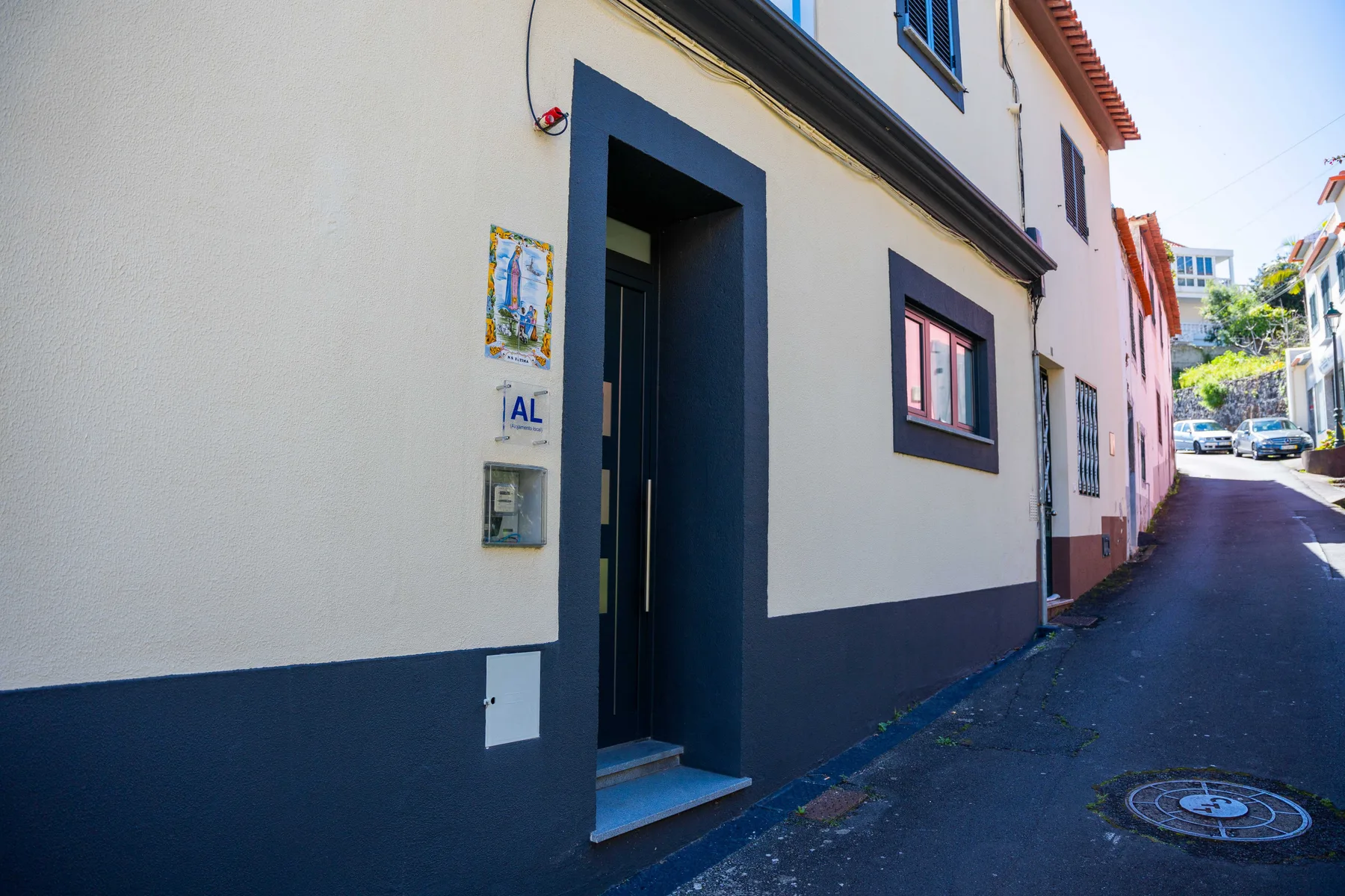 La entrada de un edificio blanco con molduras azul oscuro da a una calle estrecha.