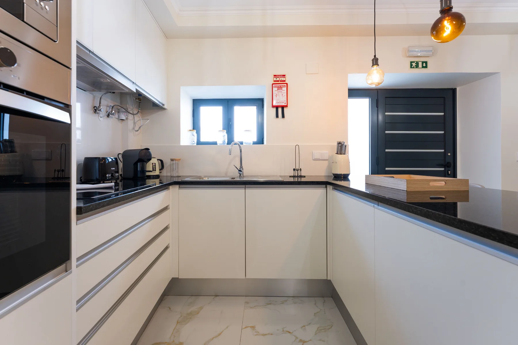 Una cocina moderna con gabinetes blancos, encimeras oscuras y un fregadero bajo la ventana.