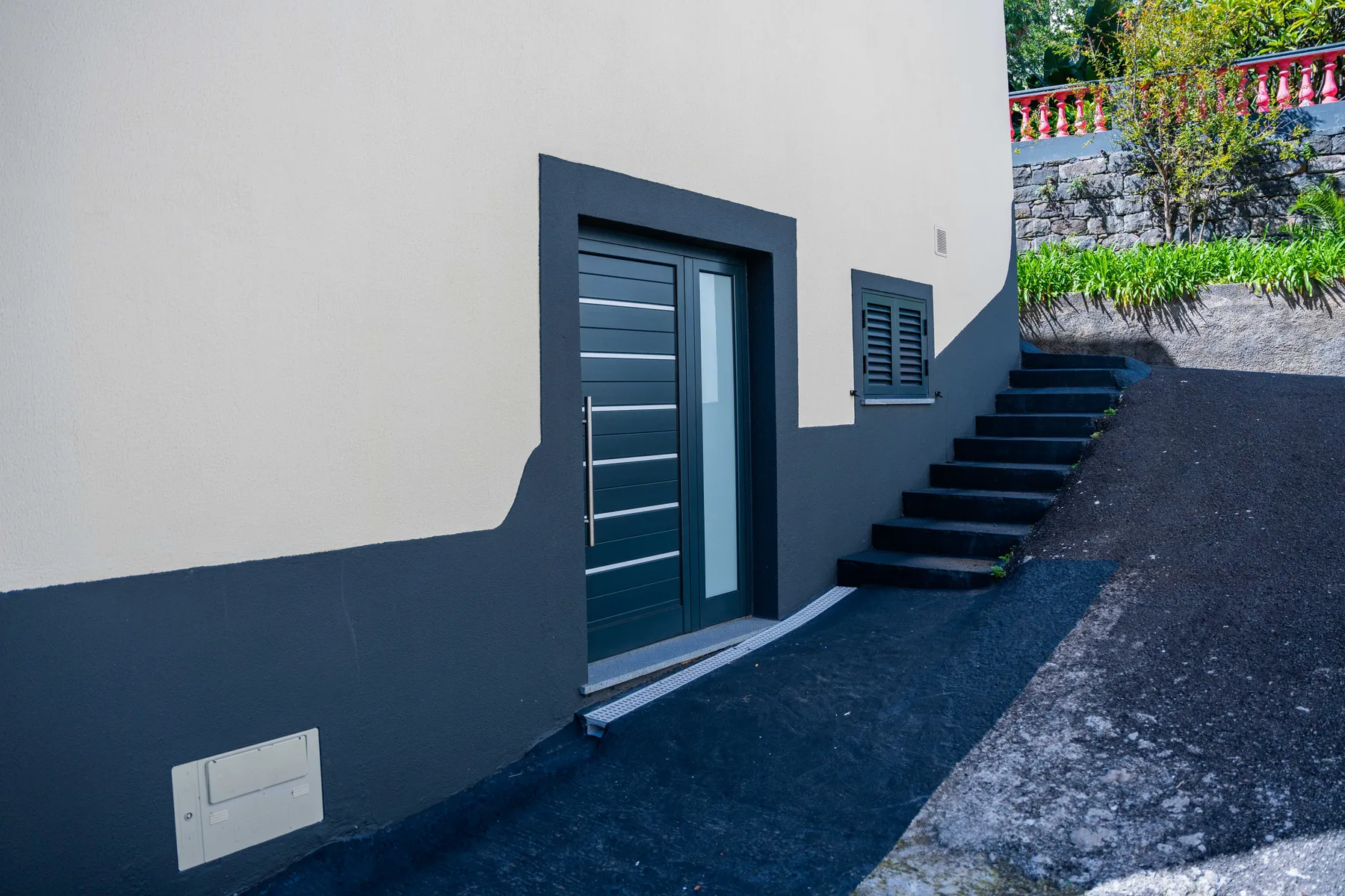 Una puerta de entrada oscura junto a escalones exteriores y una pequeña ventana con contraventanas.