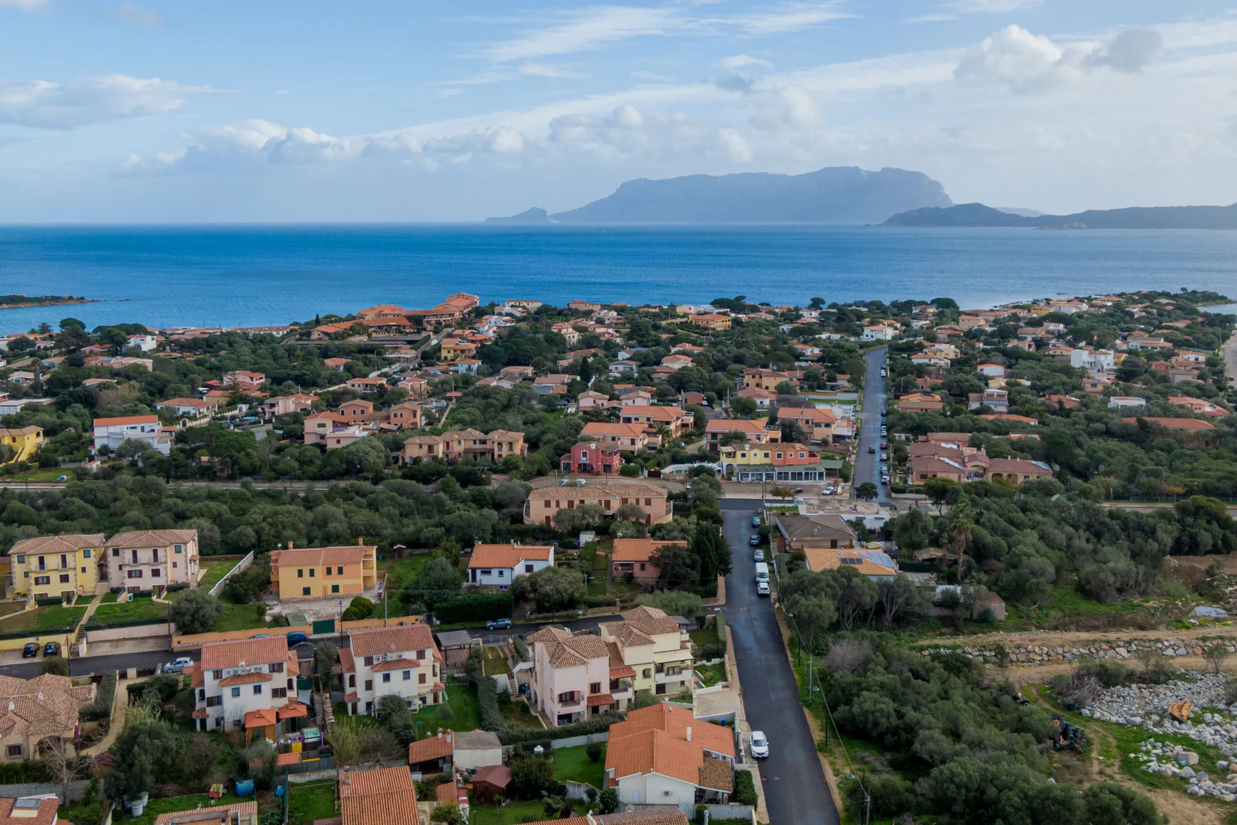 Un pueblo costero con casas entre vegetación, el mar y una isla lejana.
