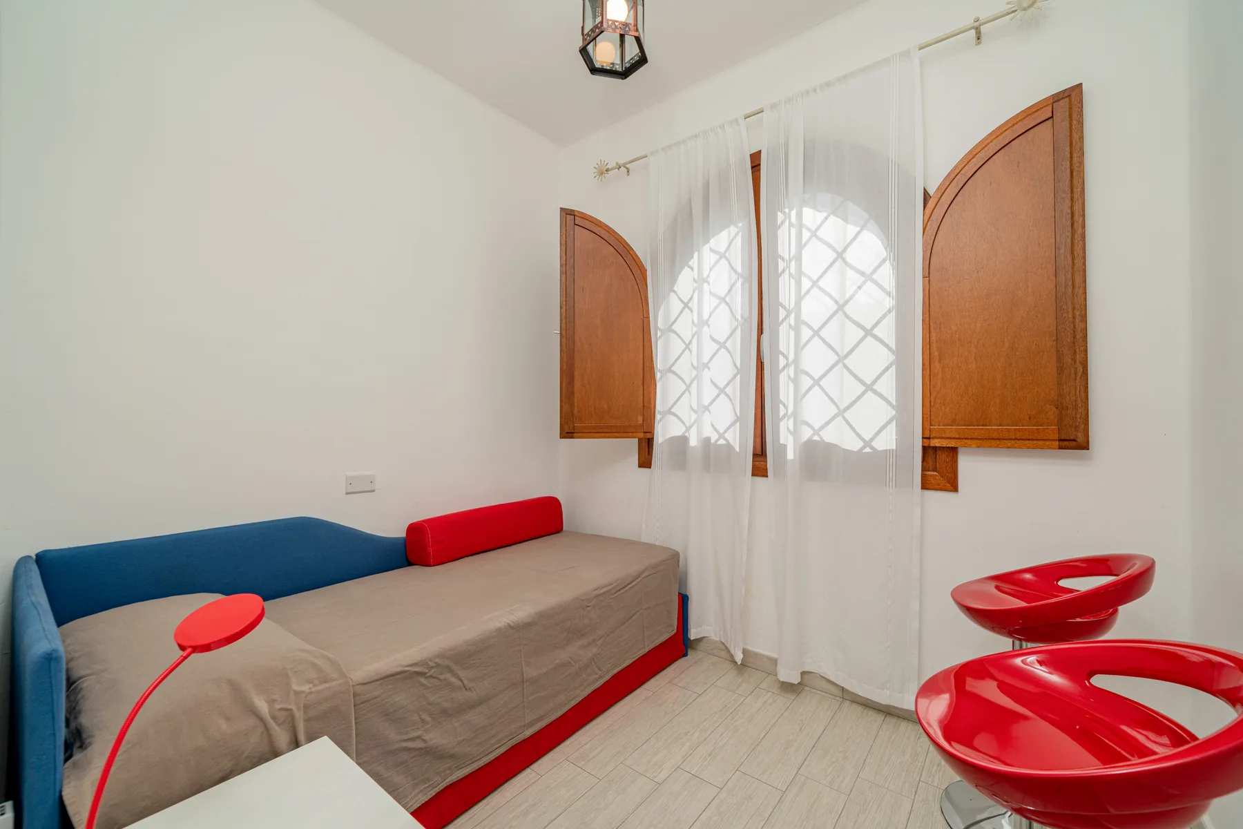 Un dormitorio con una cama bajo una ventana con cortinas blancas.