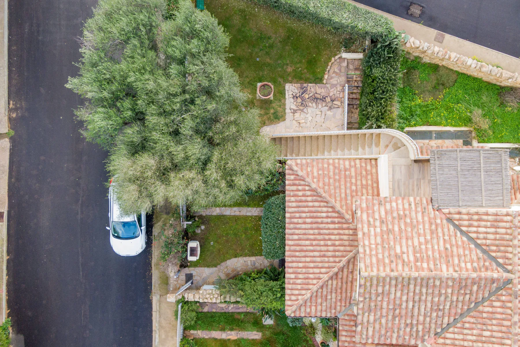 Vista aérea de una casa con tejado de tejas junto a un jardín frondoso y una carretera.