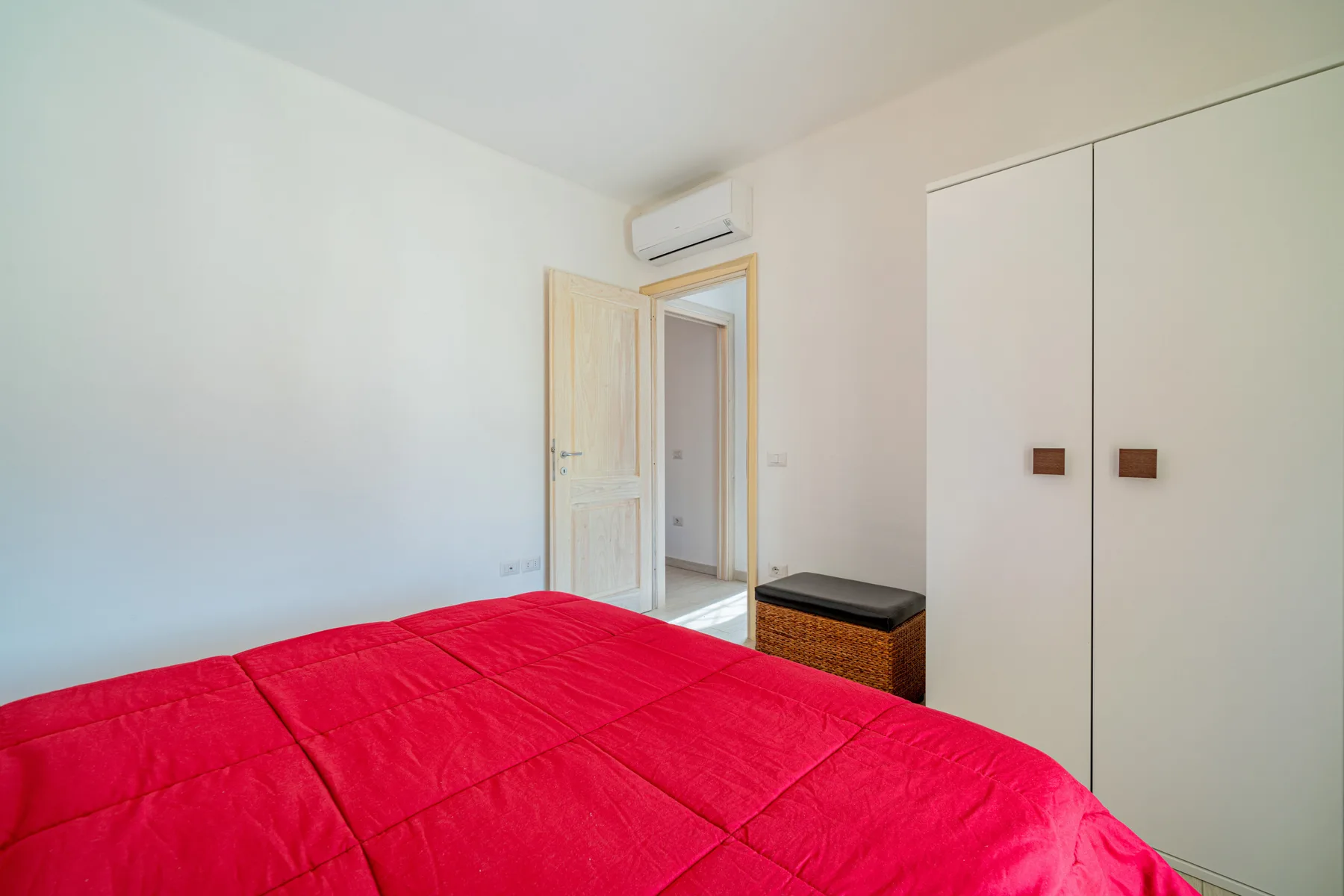 Un dormitorio con una colcha roja y una puerta abierta.