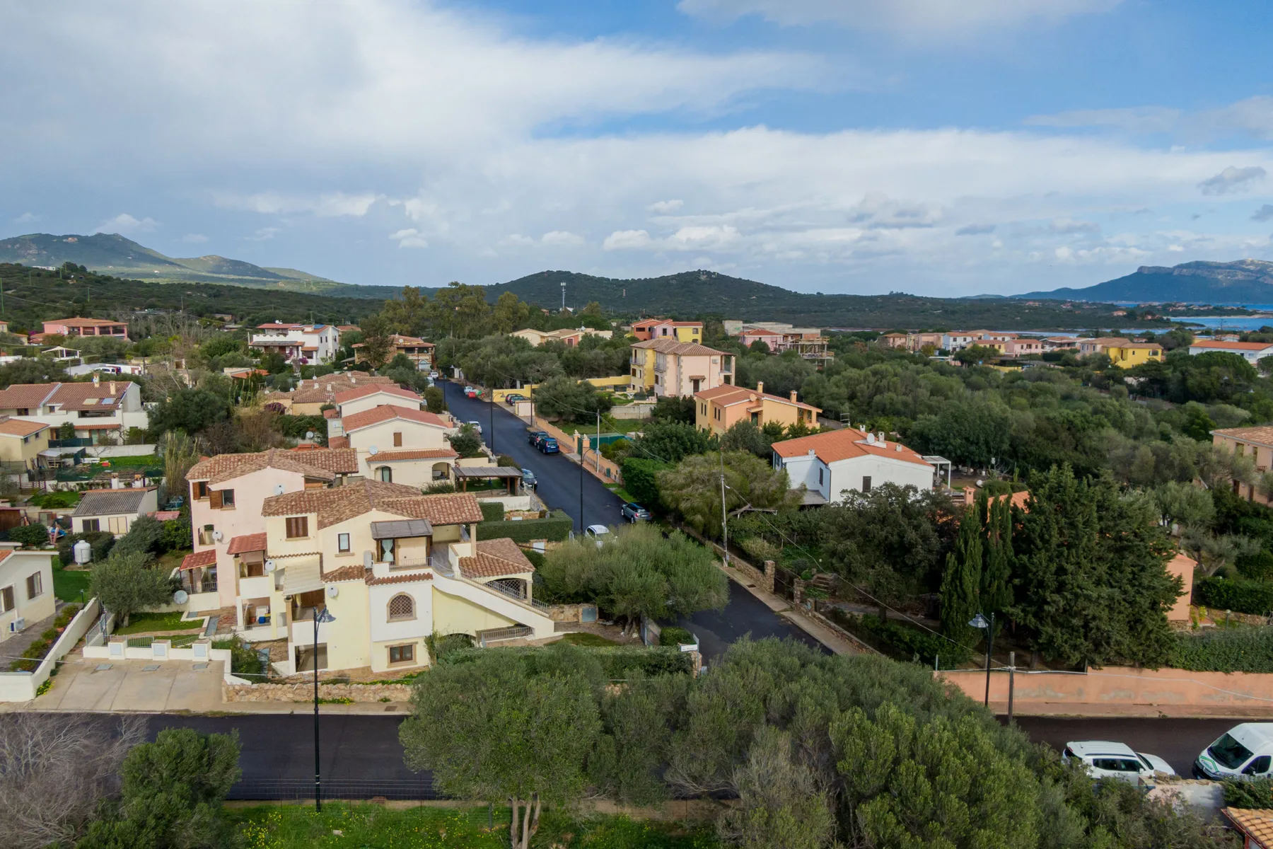 Vista aérea de un barrio residencial con casas, vegetación y colinas al fondo.