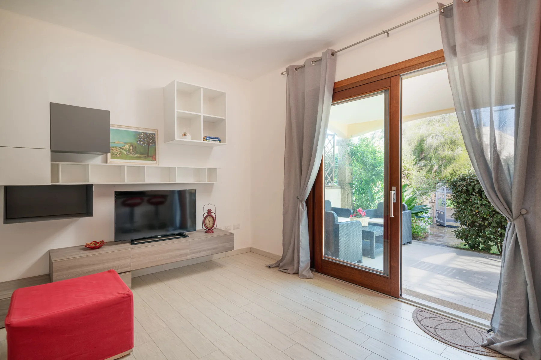 Una sala luminosa con mueble para televisión y puertas de vidrio que dan a un patio.