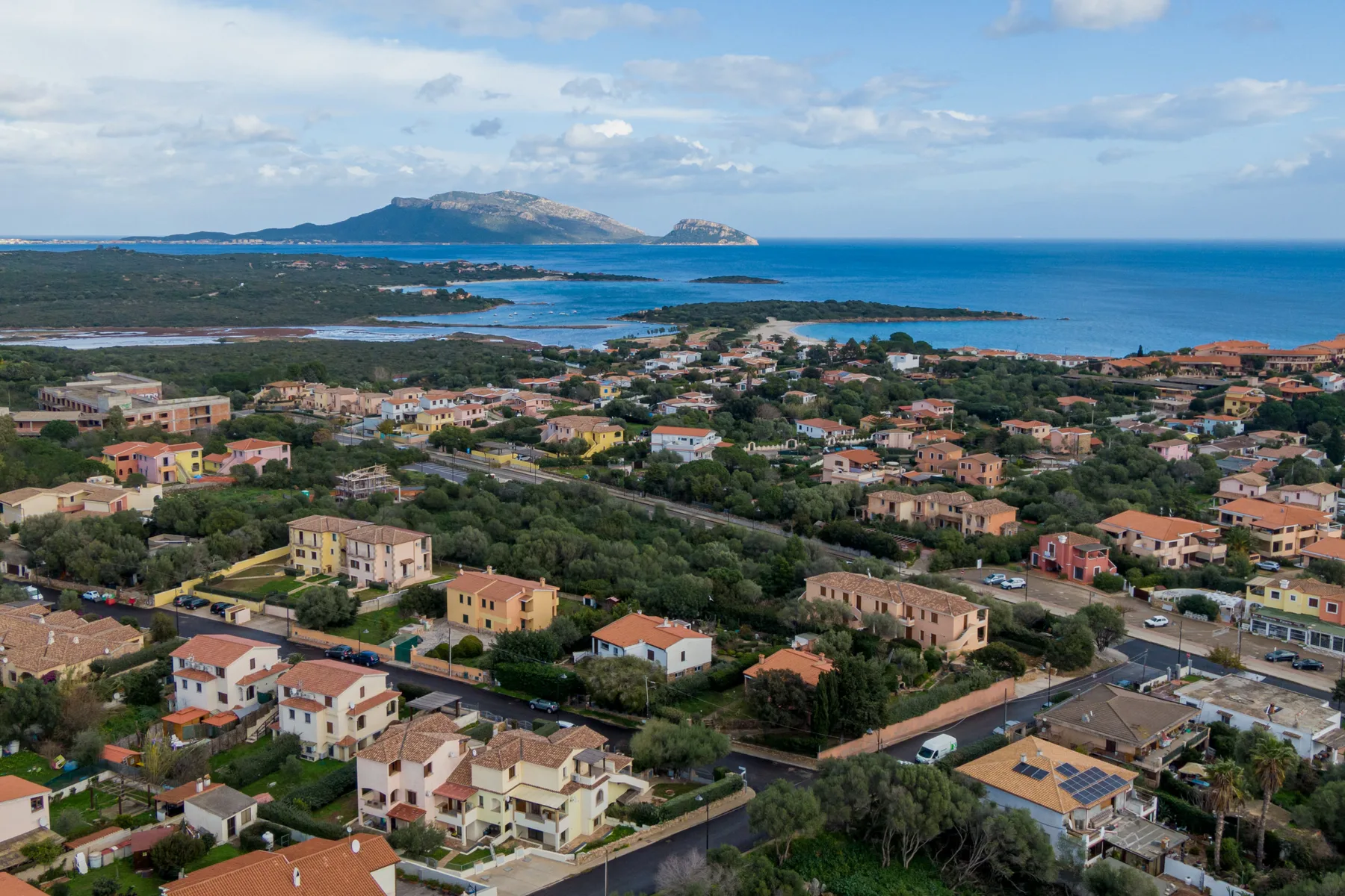 Vista aérea de un pueblo costero con casas, vegetación y agua azul.
