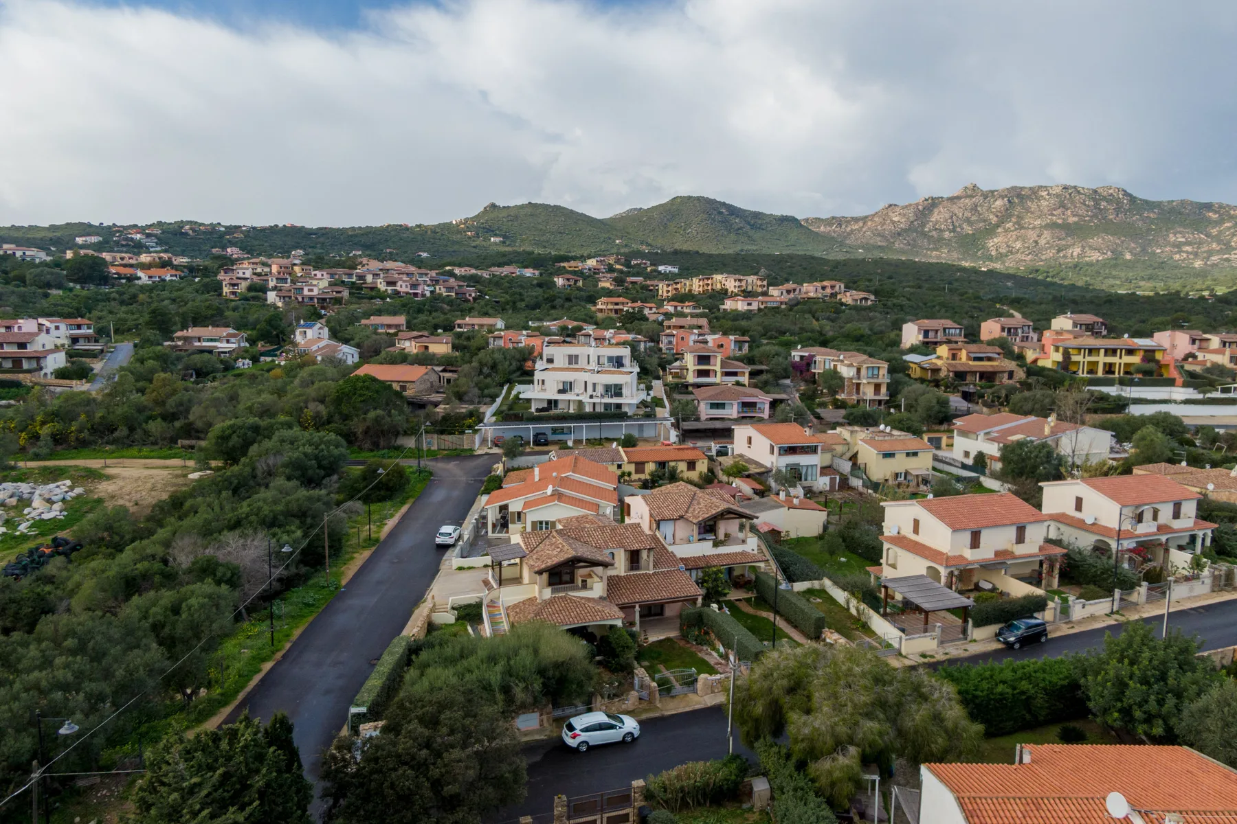 Un vecindario en una ladera con casas, calles y colinas verdes bajo un cielo nublado.
