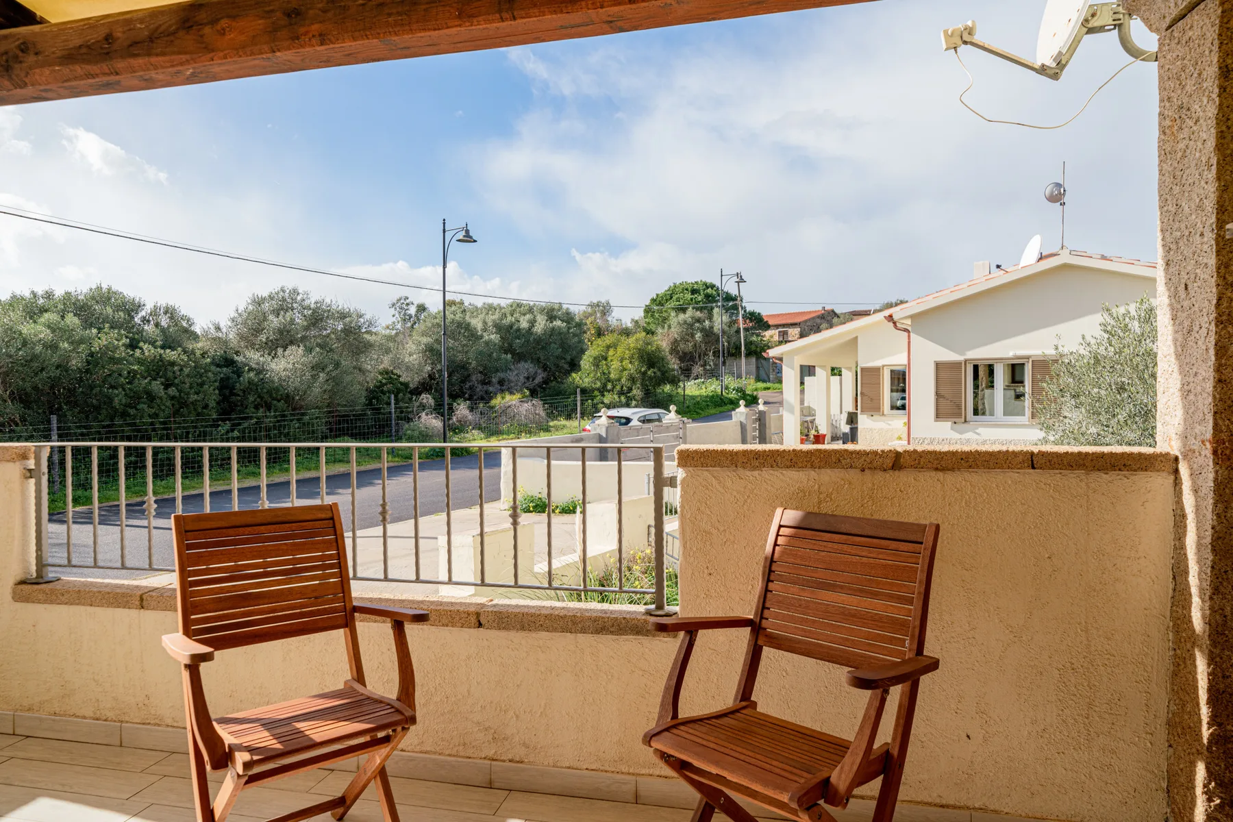 Una terraza cubierta da a una carretera, árboles y casas cercanas.