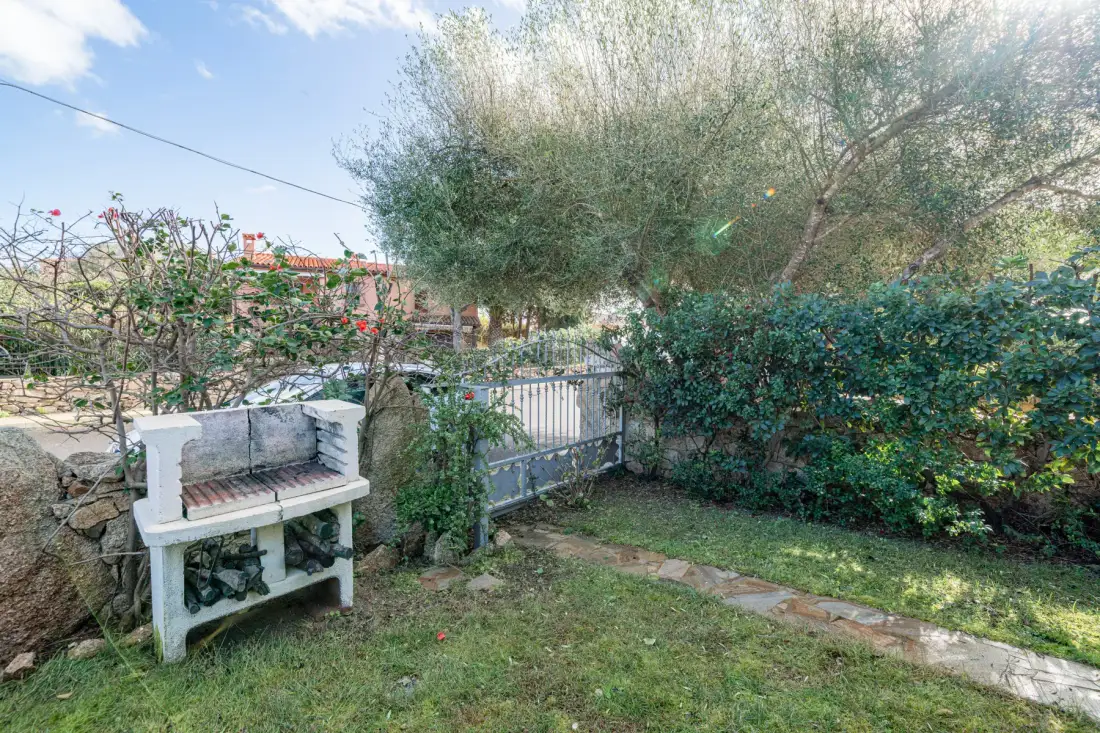 Un patio ajardinado con una barbacoa al aire libre, arbustos frondosos y un sendero de piedra.