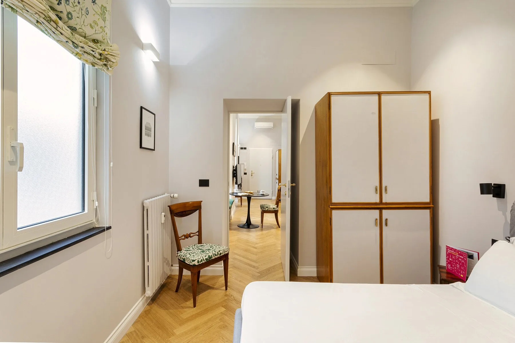 A bright bedroom with a bed, wardrobe, and window overlooking the room.