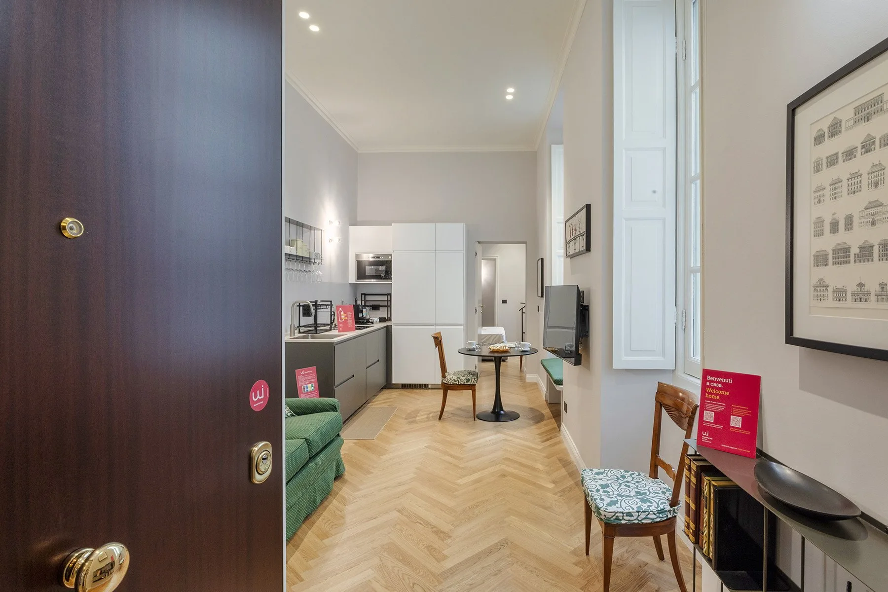 A bright living area with a compact kitchen, dining table, and green seating.