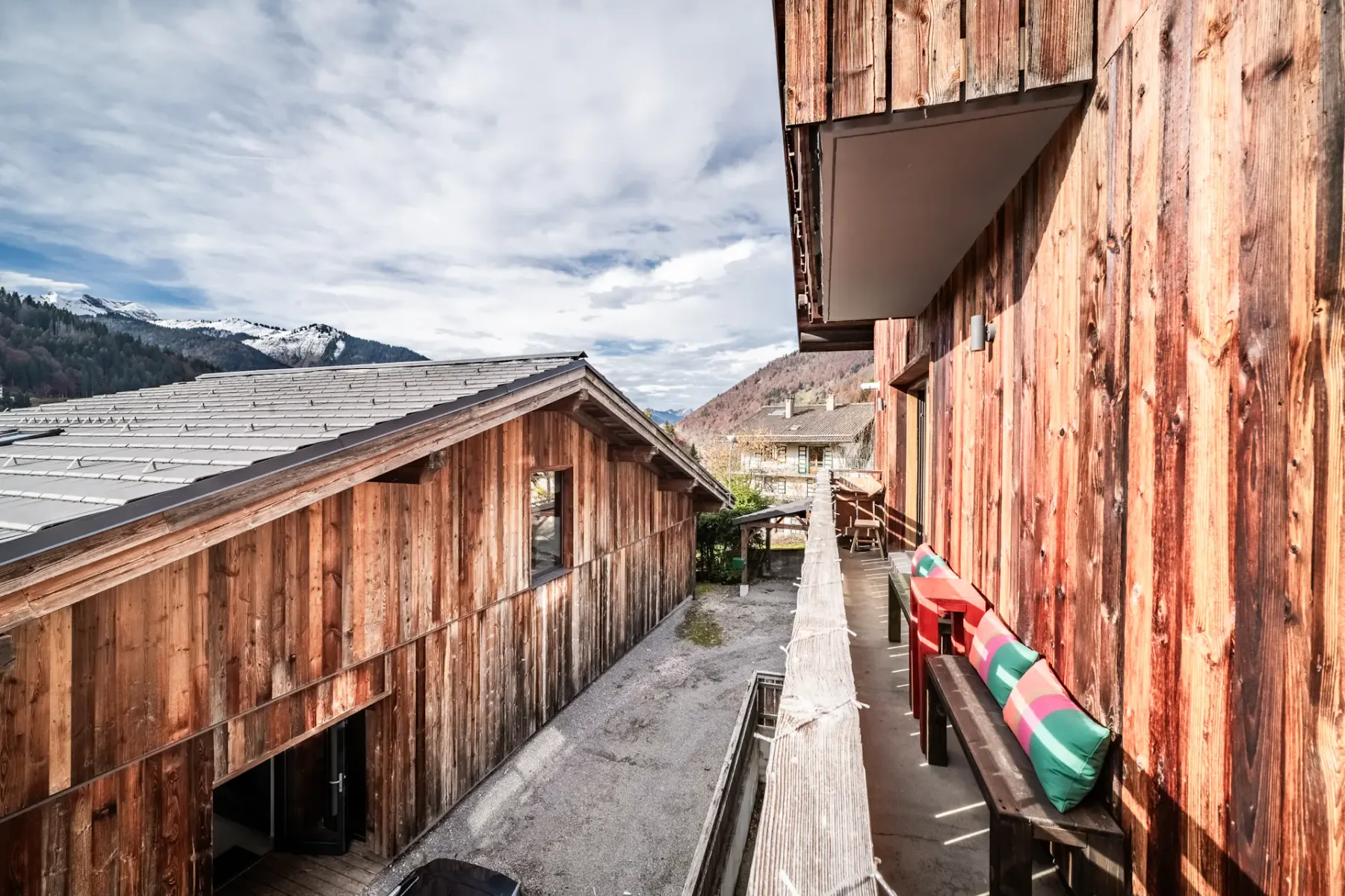 View from a balcony of rustic wooden buildings with mountains in the background under a partly cloudy sky.
