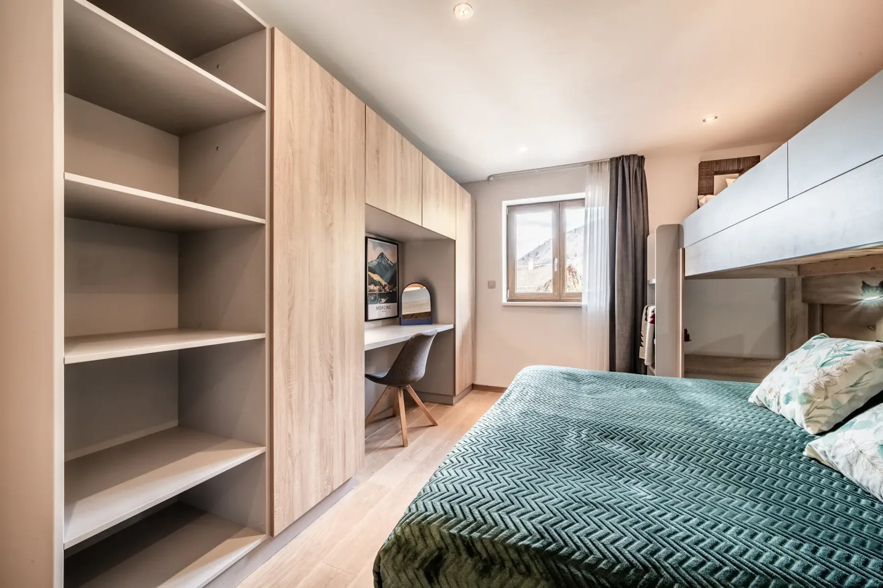 Modern bedroom with a bunk bed, green textured bedspread, built-in wooden shelves, a desk with a chair, and a window letting in natural light.