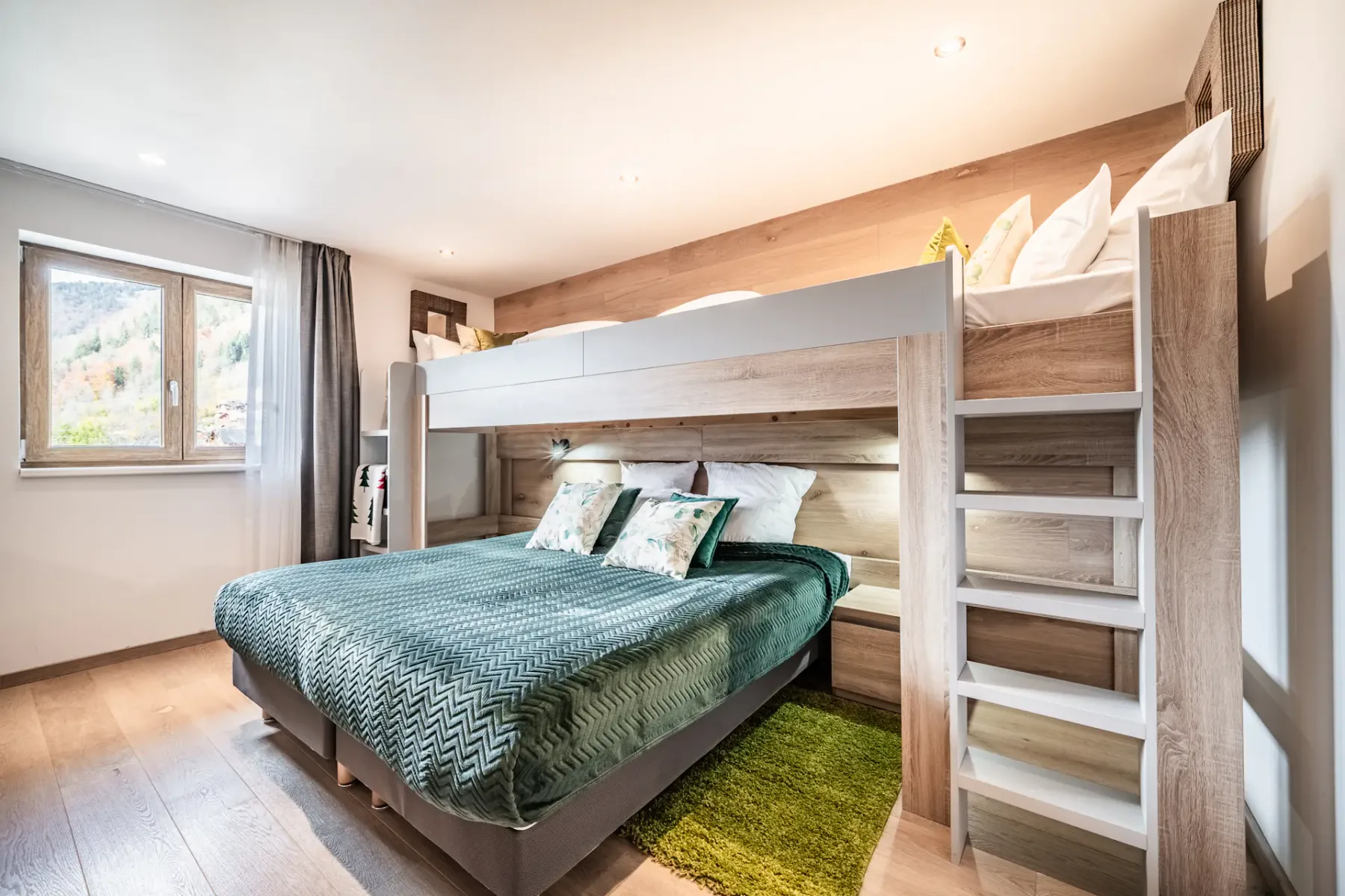Modern bedroom with a double bed below and a single loft bed above, wooden accents, green bedding, and a window letting in natural light.