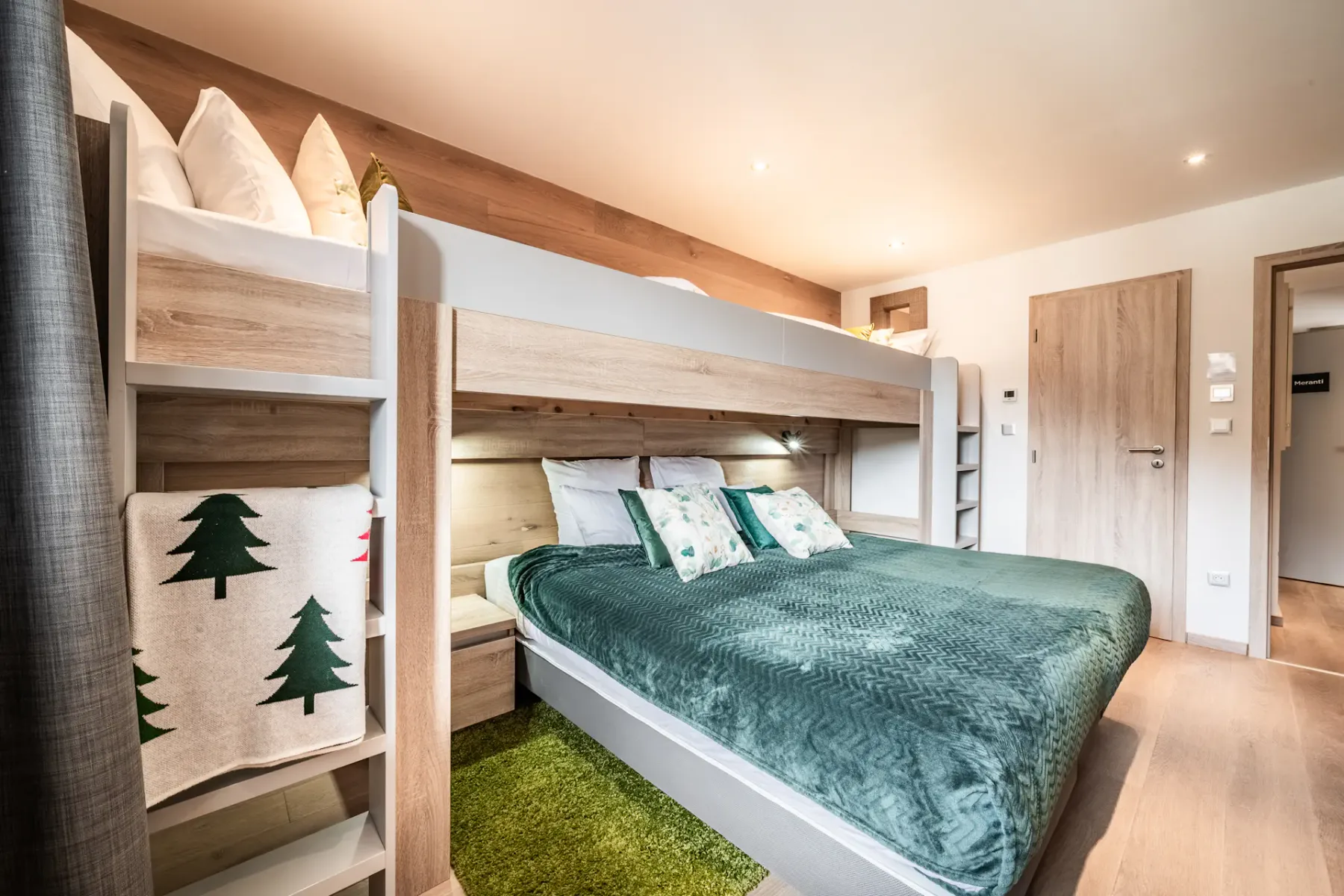 A modern bedroom with a double bed below and a single bunk bed above, green bedding, wooden accents, and a small green rug on the floor.