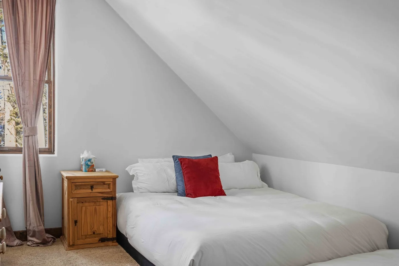 A bedroom with a bed beneath a sloped ceiling and a window.