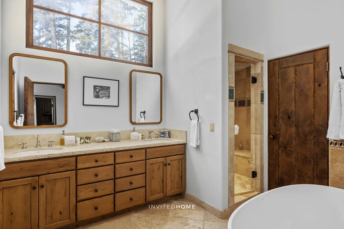 A bathroom vanity with wooden cabinetry sits beneath a large window.