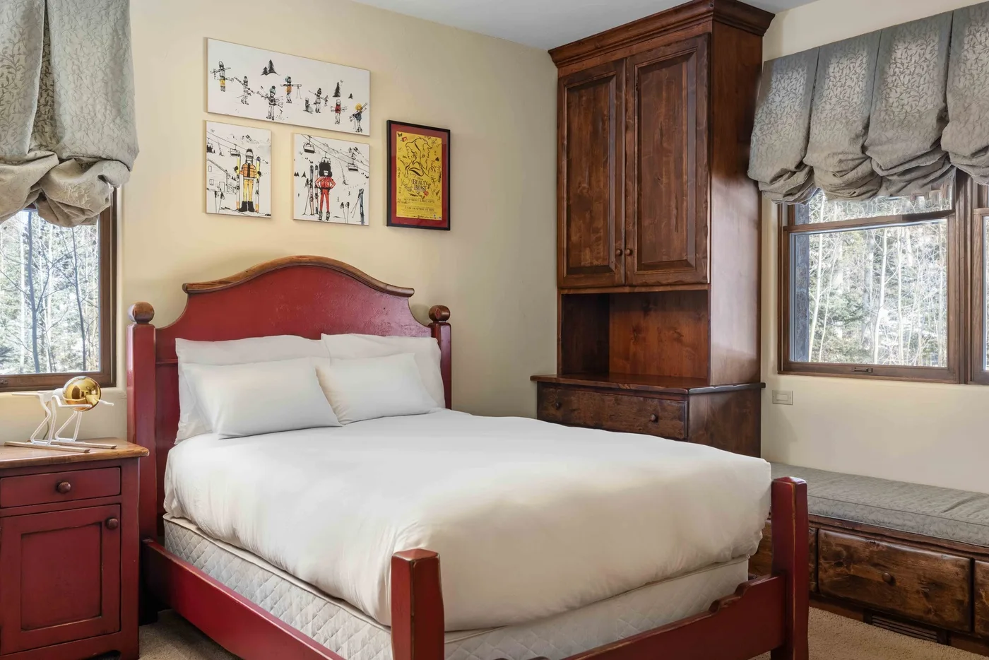 A bedroom with a red wooden bed, white bedding, and framed wall art.
