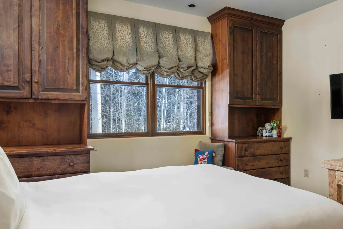 A bedroom with a bed beneath a wide window and wooden cabinetry.