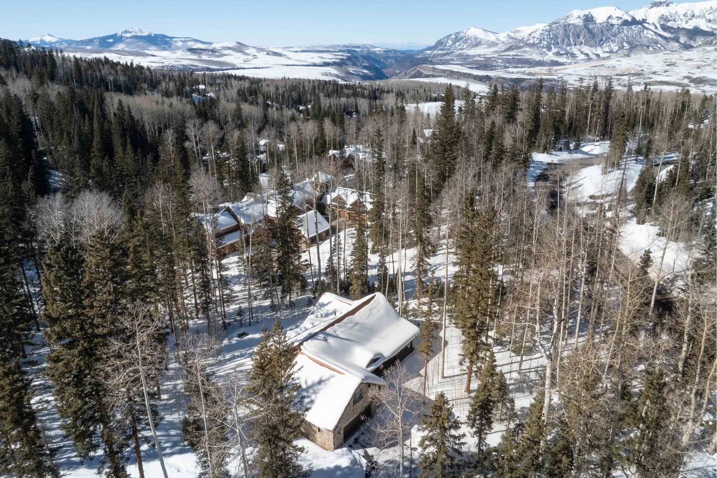 Snow-covered cabins sit among forested hills, with snowy mountain peaks in the distance.