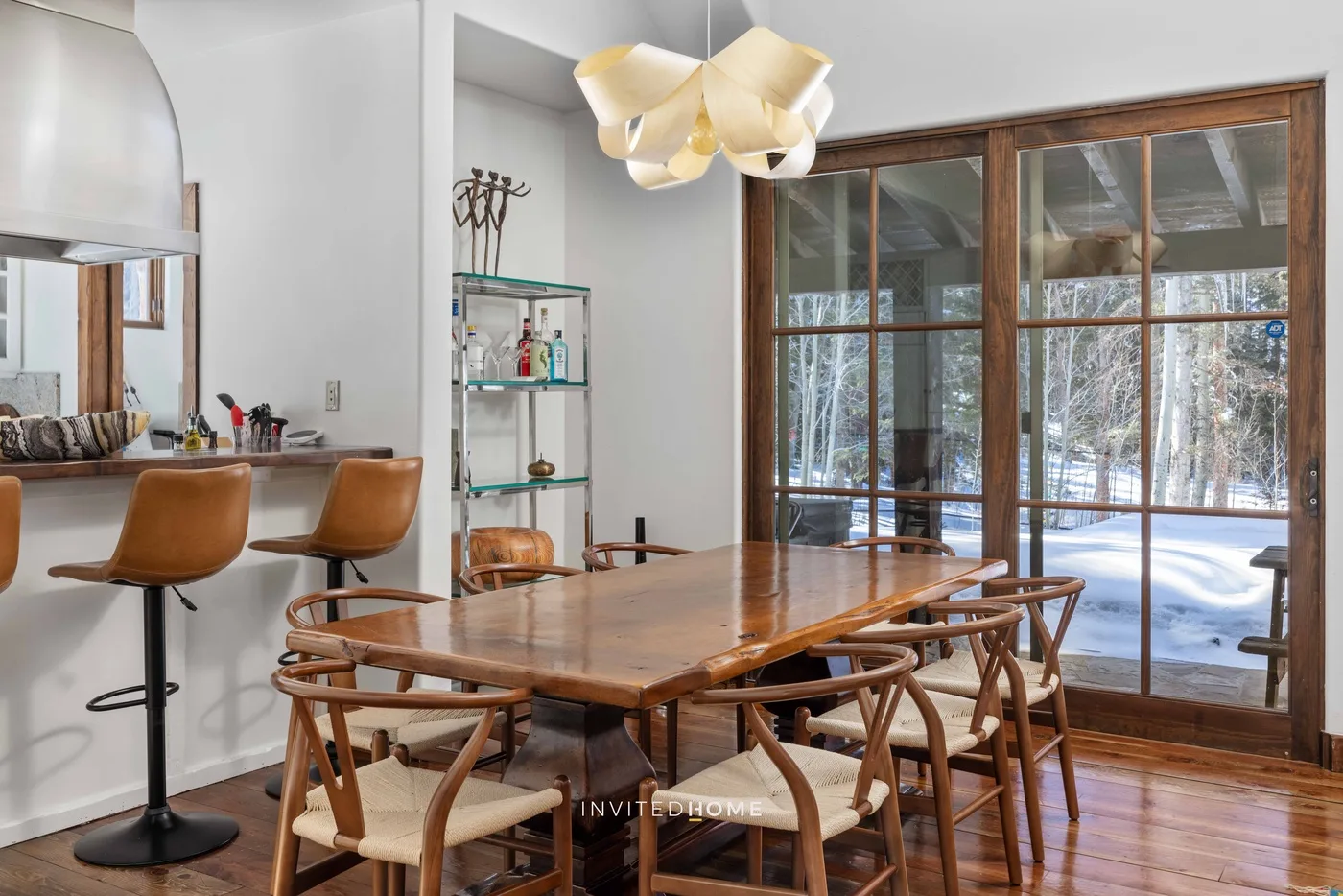 A dining room with a wooden table and chairs beside large windows.