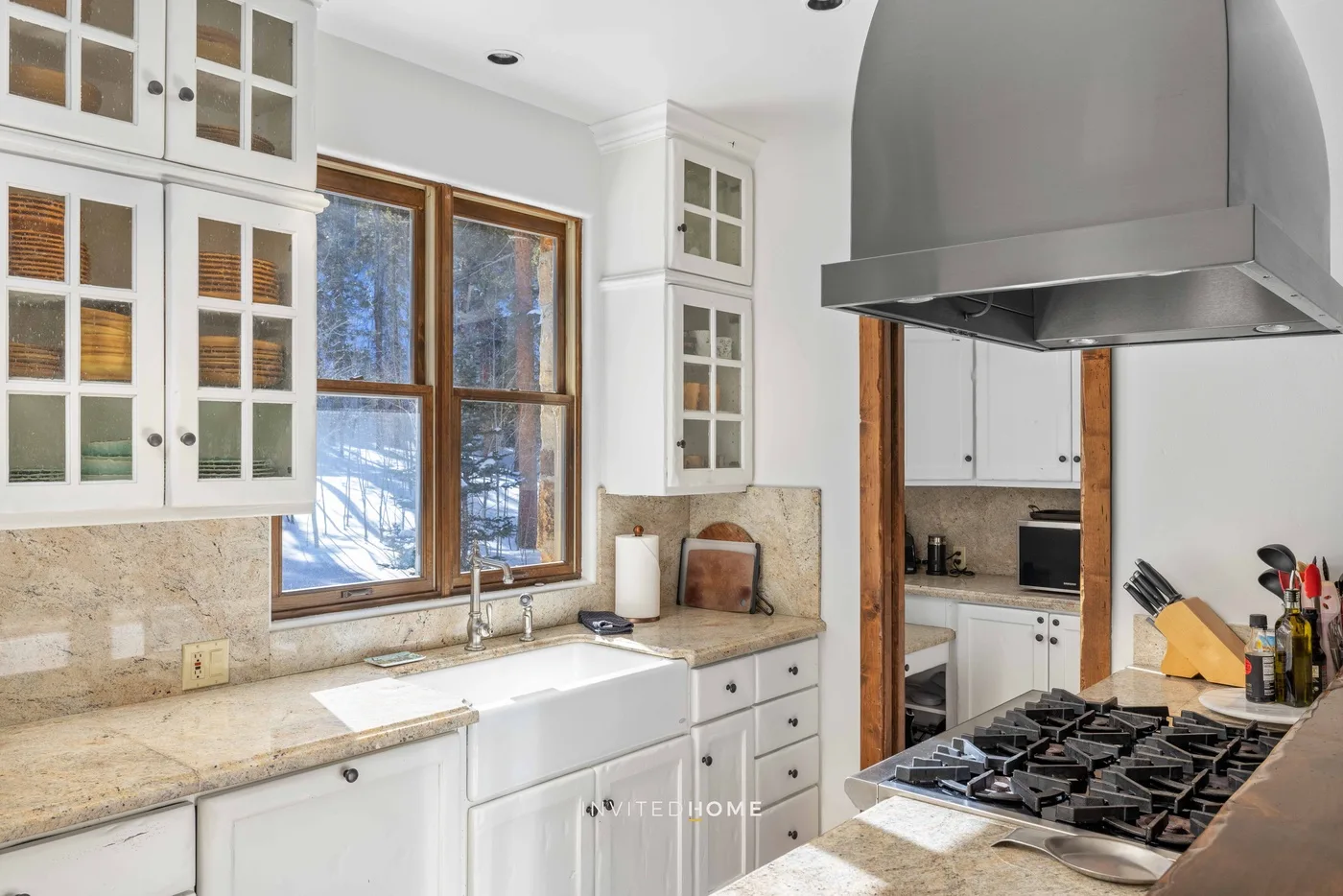 A bright kitchen with white cabinets, stone countertops, and a large range hood.