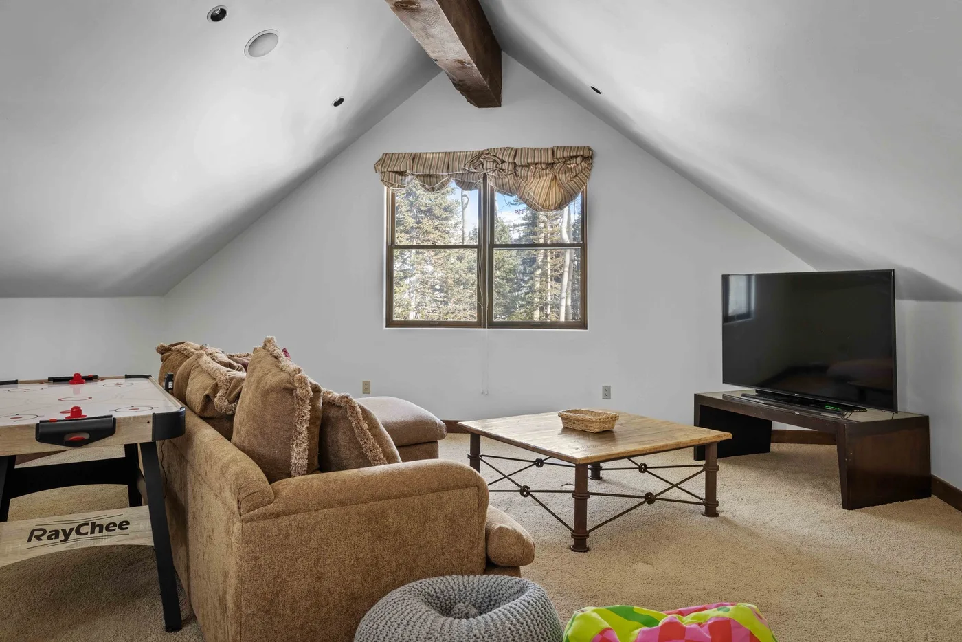 A living room with a seating area, coffee table, and television beneath a sloped ceiling.