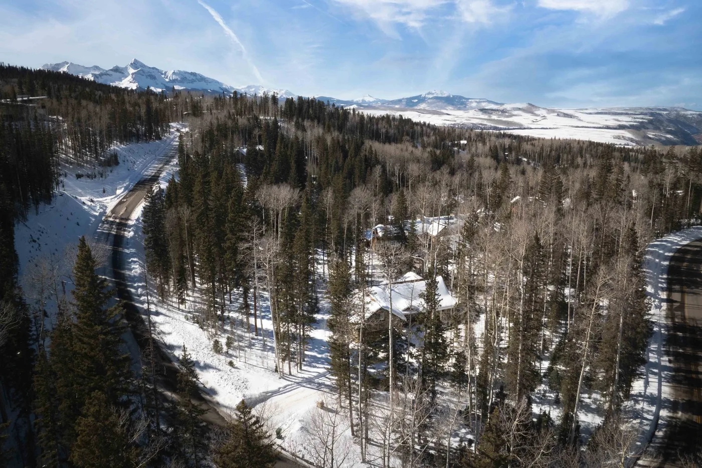 A snowy forest surrounds a small cluster of buildings, with mountains in the distance.