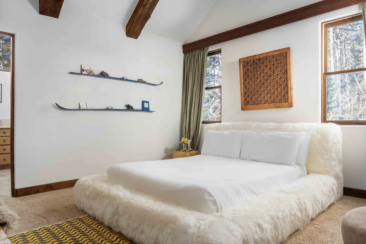 A bedroom with a bed beneath two windows and decorative shelves.