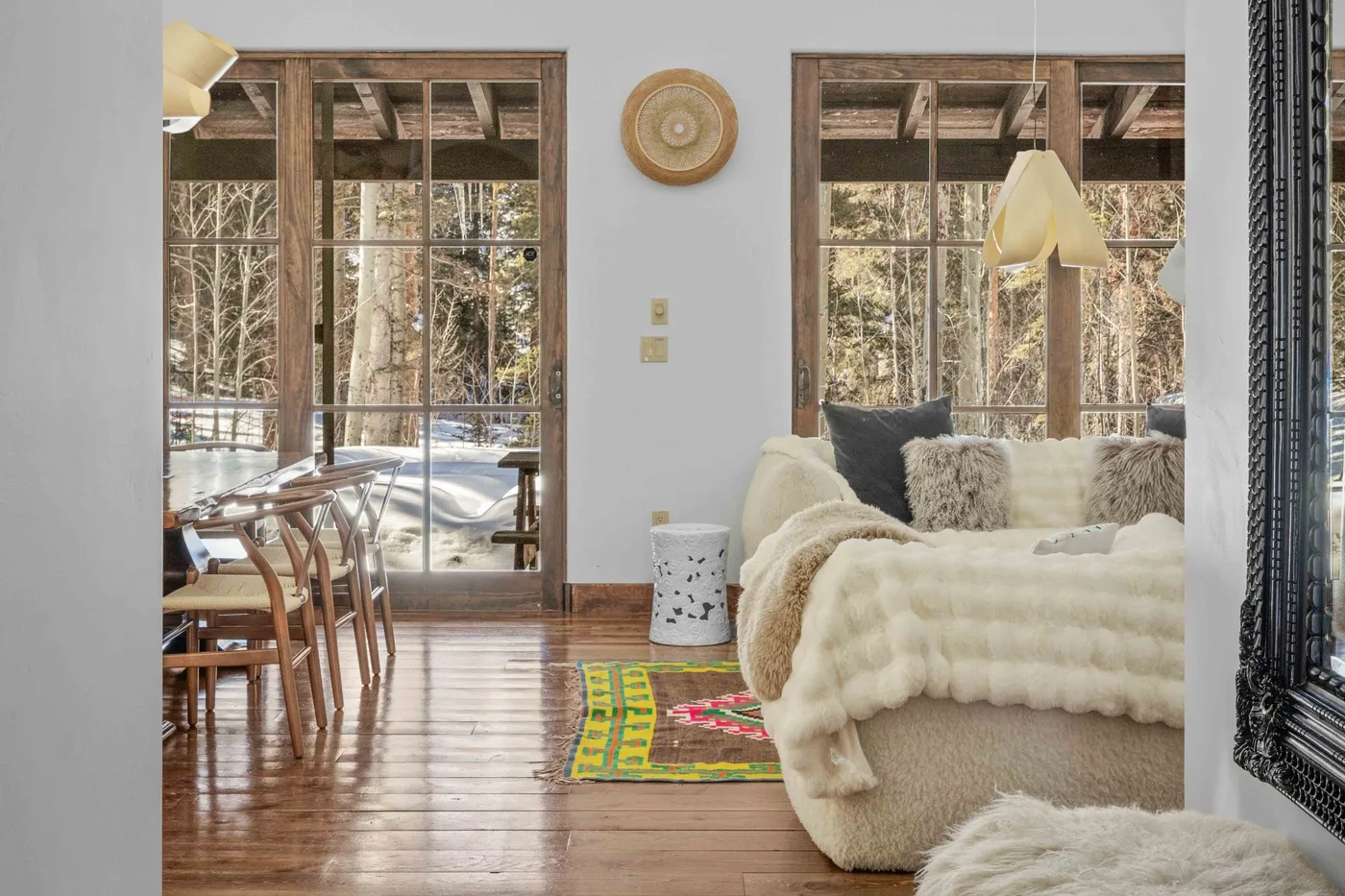 A bright living and dining area has large windows overlooking a snowy wooded landscape.
