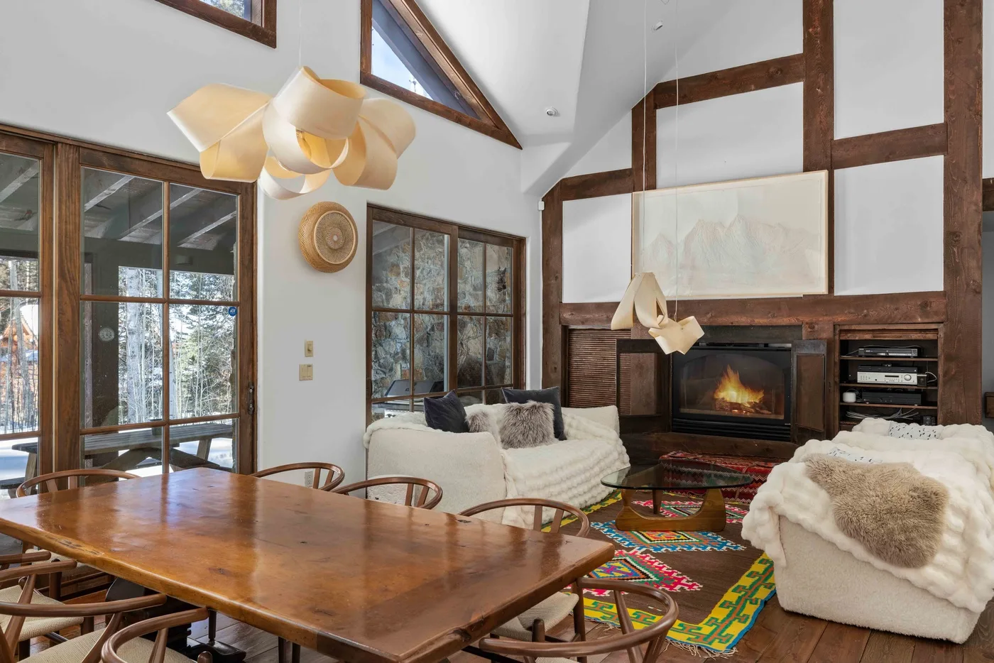 A vaulted living and dining area with a fireplace, a wooden table, and seating.