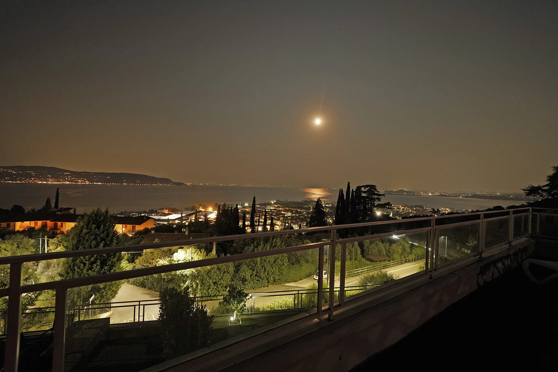 Una terraza nocturna da a un paisaje costero iluminado y al agua.