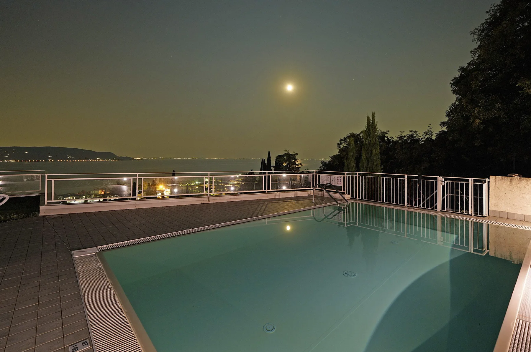 Una piscina de noche da a luces lejanas bajo una luna brillante.